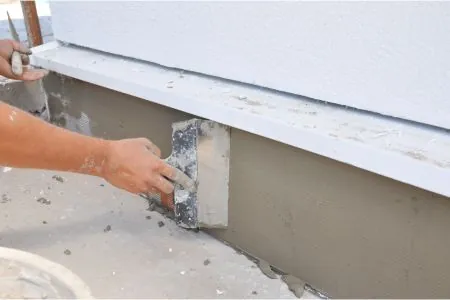 a contractor is plastering, repairing stucco house foundation